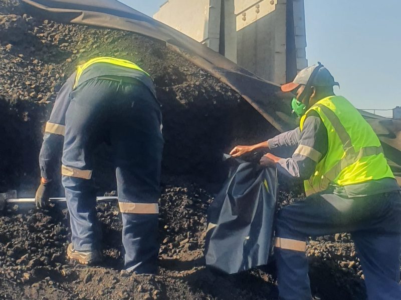 Two workers in hi-vis bagging a coal sample at a stockpile