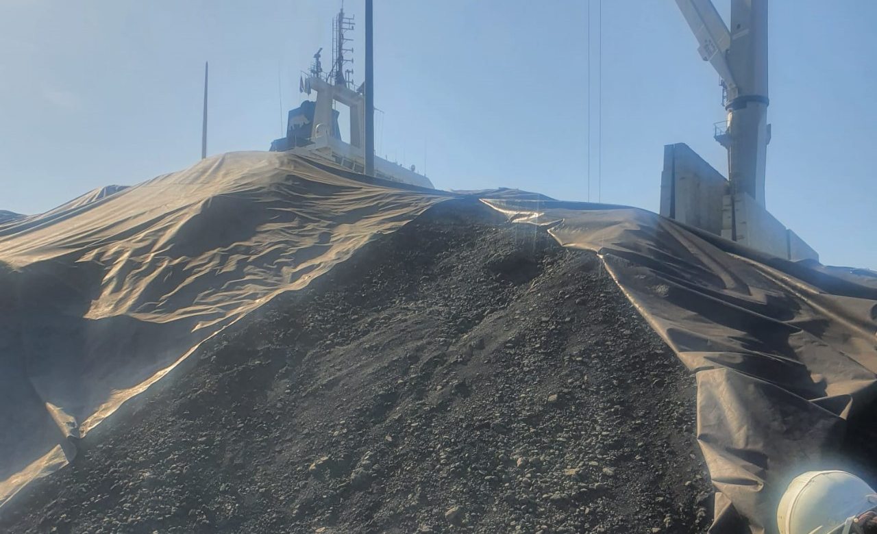 Tarped coal stockpile with a ship and crane behind it